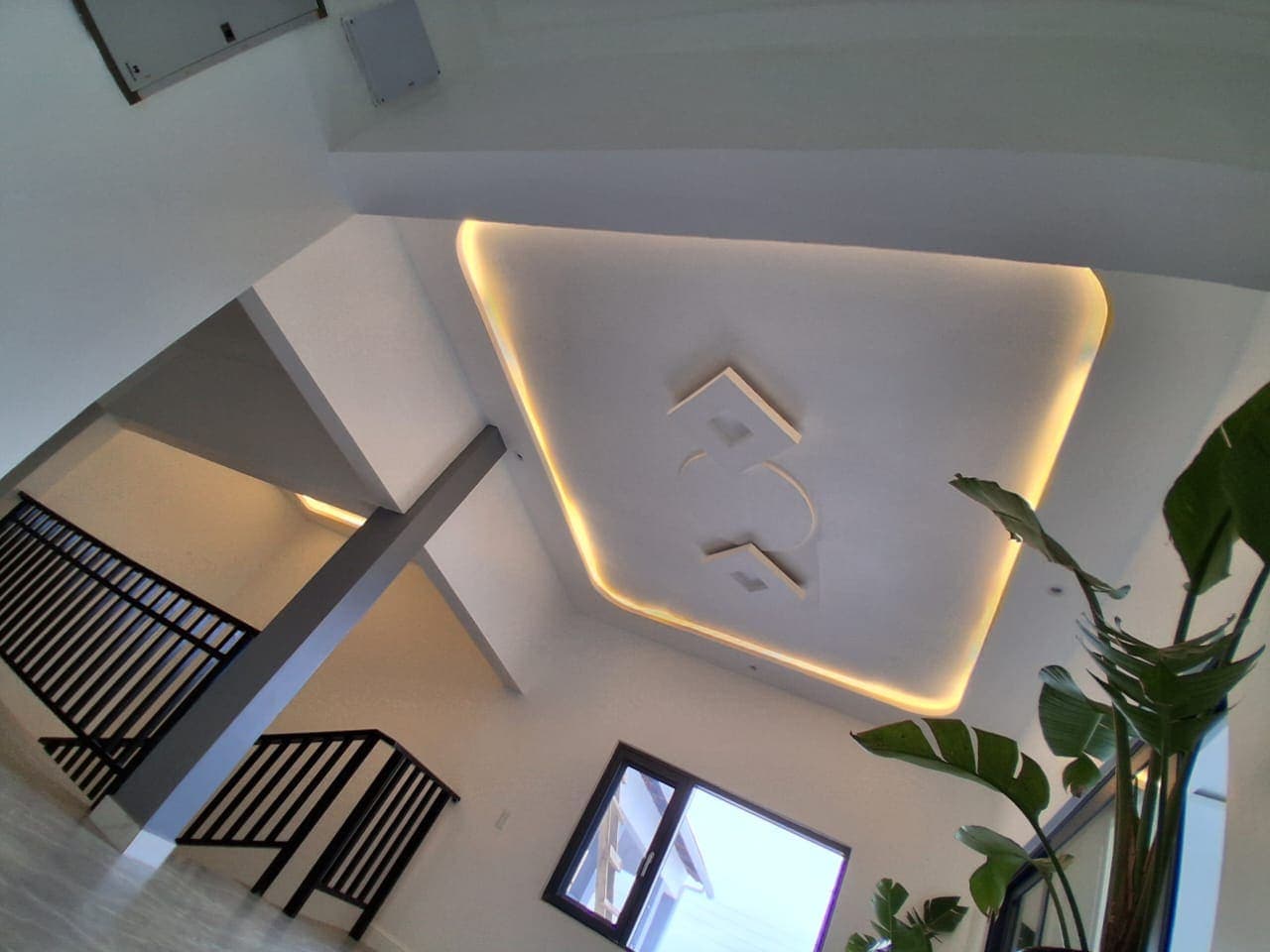 Double-height stairwell in Keta with a raised POP ceiling panel, cut-out motif, and concealed cove lighting