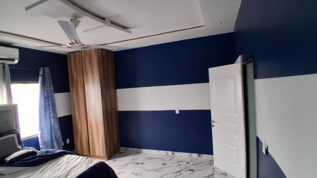 Bedroom in Keta painted in banded navy and white, with a POP ceiling, fitted wardrobe, and marble-effect tiled floor