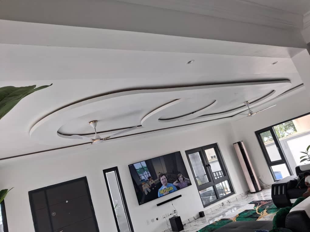 Family living room in Ghana with a sweeping curved POP ceiling relief above two ceiling fans and a wall-mounted TV