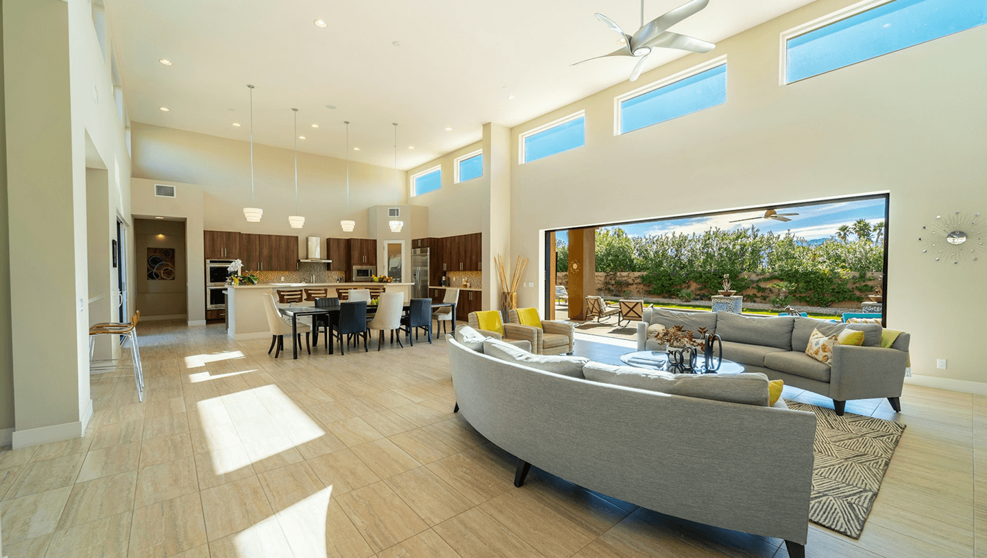 Open plan living room with a high ceiling, tiled floor and wide glass doors opening onto a garden